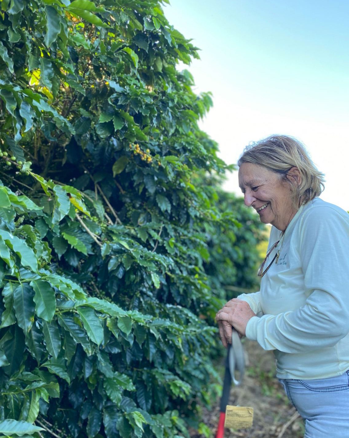 Maria Silvia Mendonça smiling beside a coffee tree at the farm
